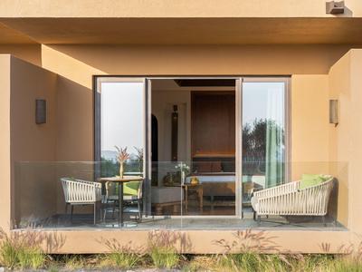 Outdoor patio with glass railing, two armchairs, and a table with flowers.