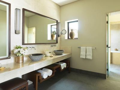 Arched corridor with wooden floor and lanterns overlooking a courtyard with wicker chairs and plants.