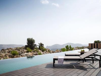 Poolside lounge chairs on wooden deck overlooking mountains and rocky landscape under clear sky.