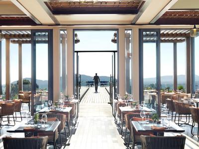 Elegant empty restaurant with wooden tables and chairs overlooking a scenic landscape.