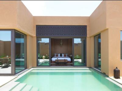 Modern hotel room with large windows opening to a private pool in a sunny courtyard.