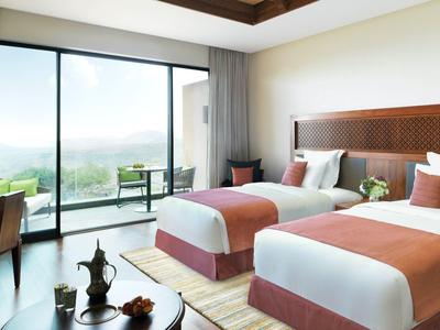 Hotel room with two beds, wooden accents, and a balcony with outdoor seating and view.