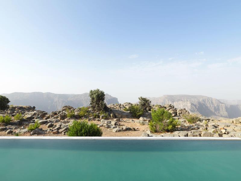 Clear pool overlooking rugged rocky landscape under a blue sky.