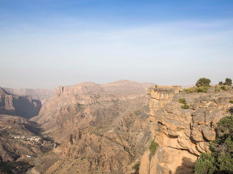 Vast rocky canyon landscape under a clear blue sky with sparse vegetation.