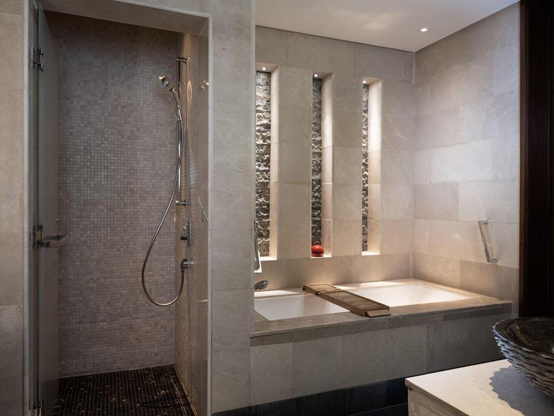 Modern hotel bathroom with a walk-in shower and a built-in bathtub under vertical windows.