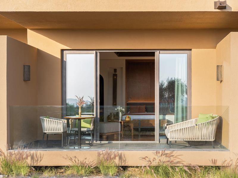 Outdoor patio with glass railing, two armchairs, and a table with flowers.
