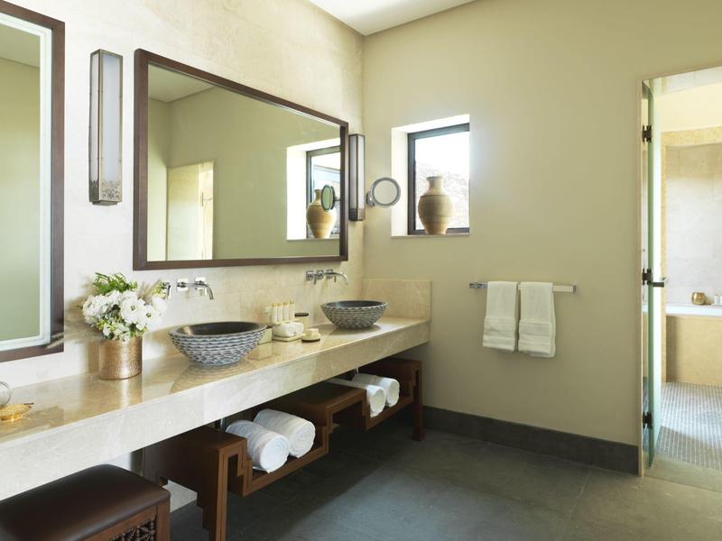 Arched corridor with wooden floor and lanterns overlooking a courtyard with wicker chairs and plants.