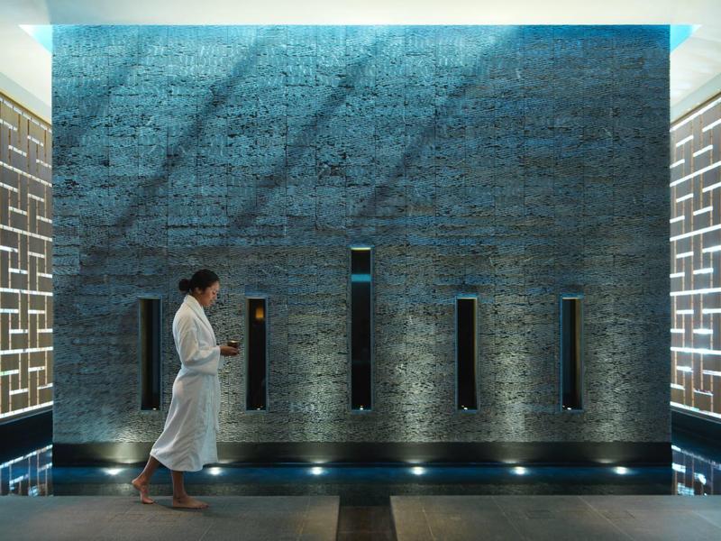 Spa corridor with bright geometric wall panels and person in white robe walking by.