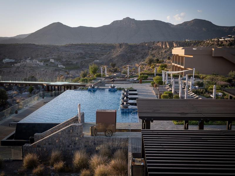 Mountain view with an infinity pool and lounge area overlooking the rocky landscape at sunset.