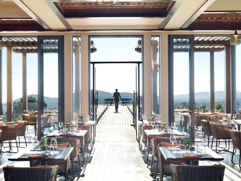 Elegant empty restaurant with wooden tables and chairs overlooking a scenic landscape.