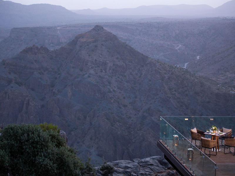 Outdoor dining terrace overlooking a vast mountain valley at dusk, with tables set for guests.