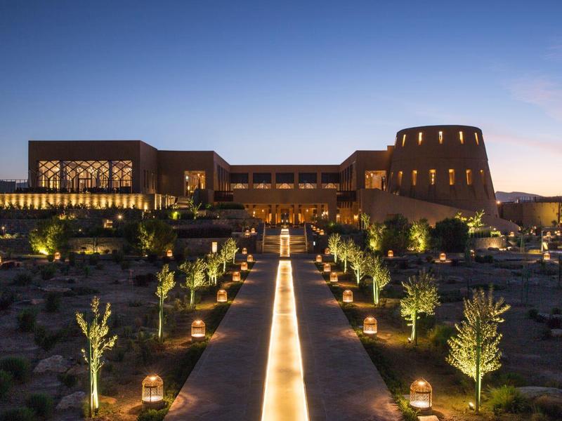 Luxurious hotel lit at dusk with a central water feature and landscaped gardens.
