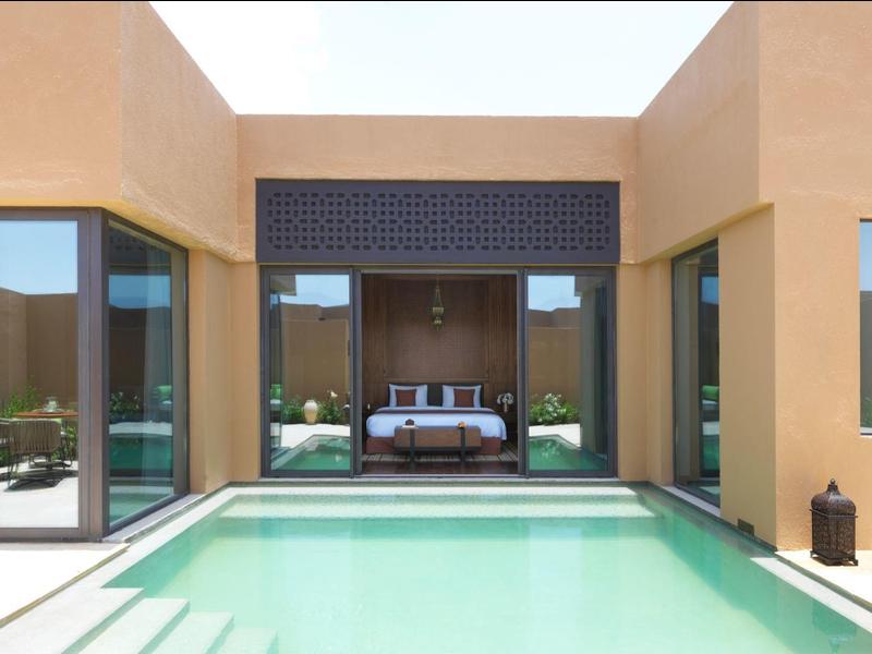 Modern hotel room with large windows opening to a private pool in a sunny courtyard.