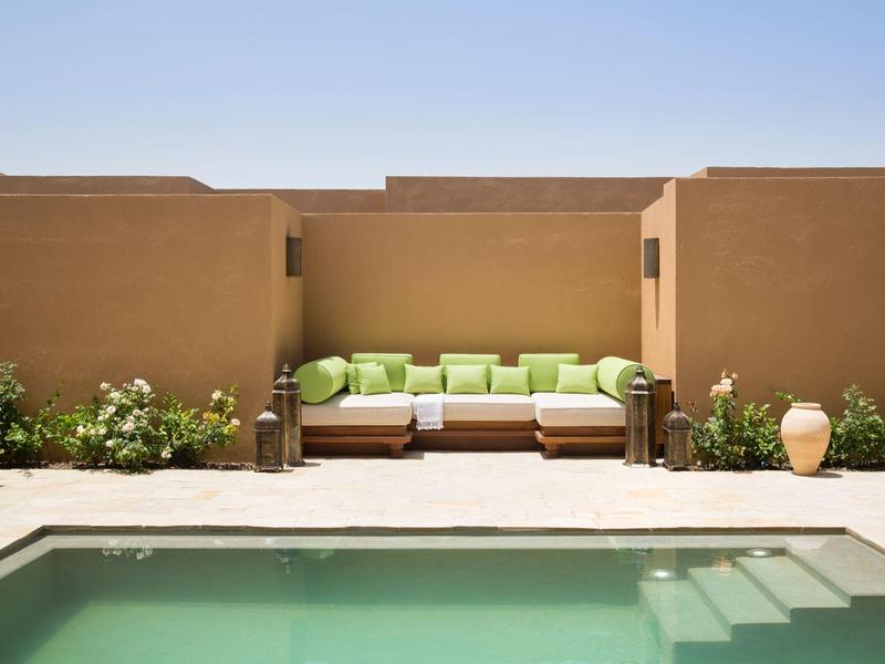 Outdoor lounge with green cushions by a pool in a modern desert-style villa