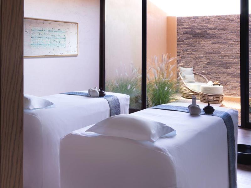 A serene spa room with two massage tables, natural light, and earthy decor.