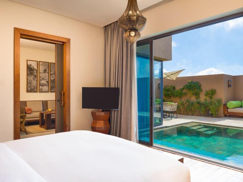 Bright hotel room with comfortable bed and open sliding door to pool and patio area.