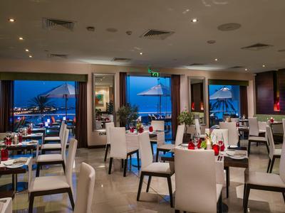 Modernes Hotelrestaurant mit weißen Stühlen und Blick auf das abendliche Meer.