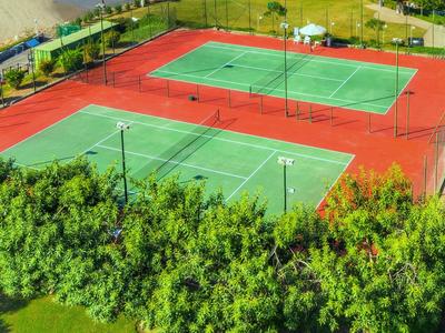 Zwei Tennisplätze in einem Hotel mit grünen Bäumen im Vordergrund.