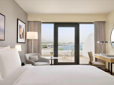 Modernes Hotelzimmer mit großem Bett, Sitzbereich und Blick auf eine Terrasse und Wasser.