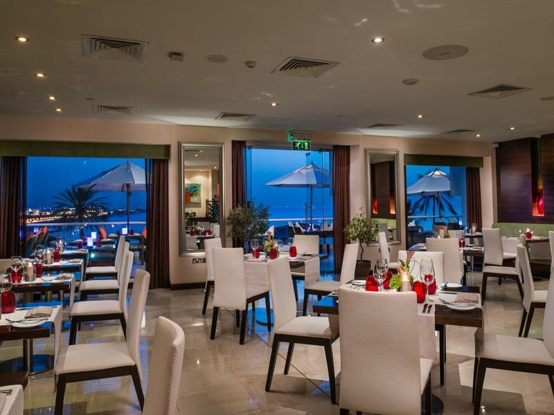 Moderner Restaurantinnenraum mit weißen Stühlen, gedeckten Tischen und Meerblick bei Dämmerung.