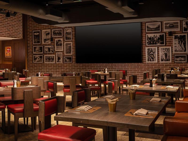 Modernes Restaurant mit roten Stühlen, Holztischen und zahlreichen Bildern an Backsteinwänden.