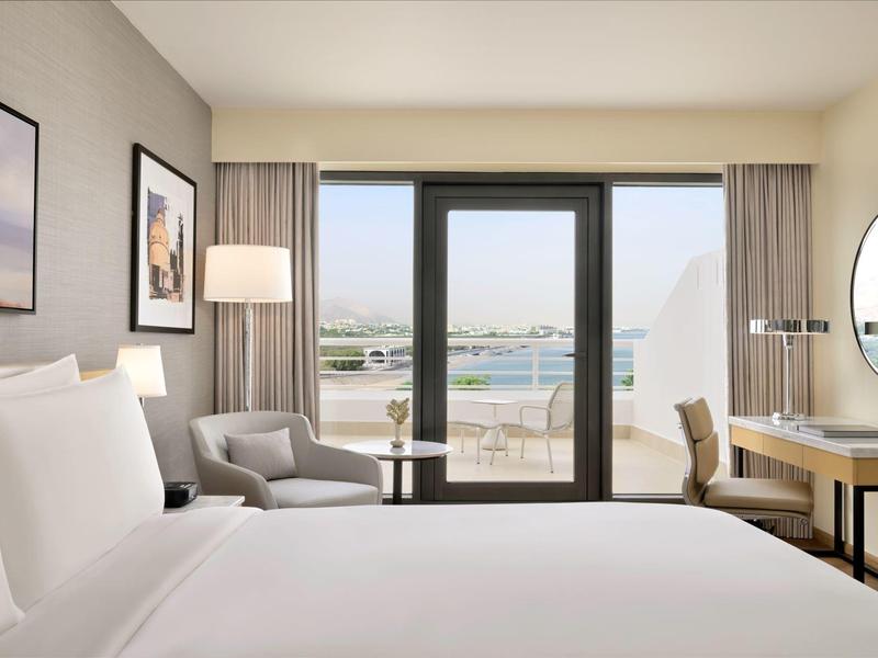 Modernes Hotelzimmer mit großem Bett, Sitzbereich und Blick auf eine Terrasse und Wasser.