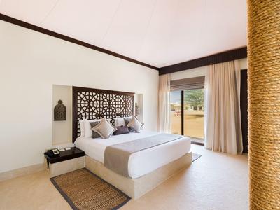 Schlafzimmer mit großem Bett, cremefarbenen Wänden, elegantem Kopfteil und Blick auf Terrasse.