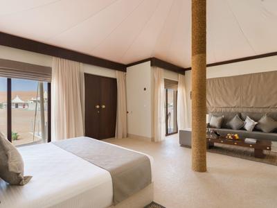 Helles Hotelzimmer mit großem Bett, Sofa und Blick auf eine Terrasse.