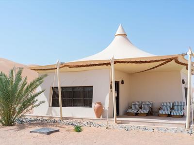 Einzelnes Zelt mit weißer spitzer Dachkonstruktion in Wüstenlandschaft bei klarem Himmel.