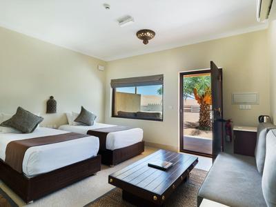 Zweibettzimmer mit Holzrahmen, großem Fenster, Zugang zur Terrasse und grauer Couch.