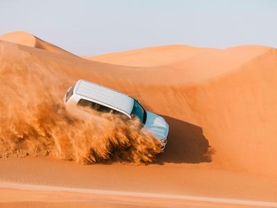 Ein weißes Geländewagenfahrzeug fährt einen Sanddünenhang hinunter und wirbelt Sand auf.