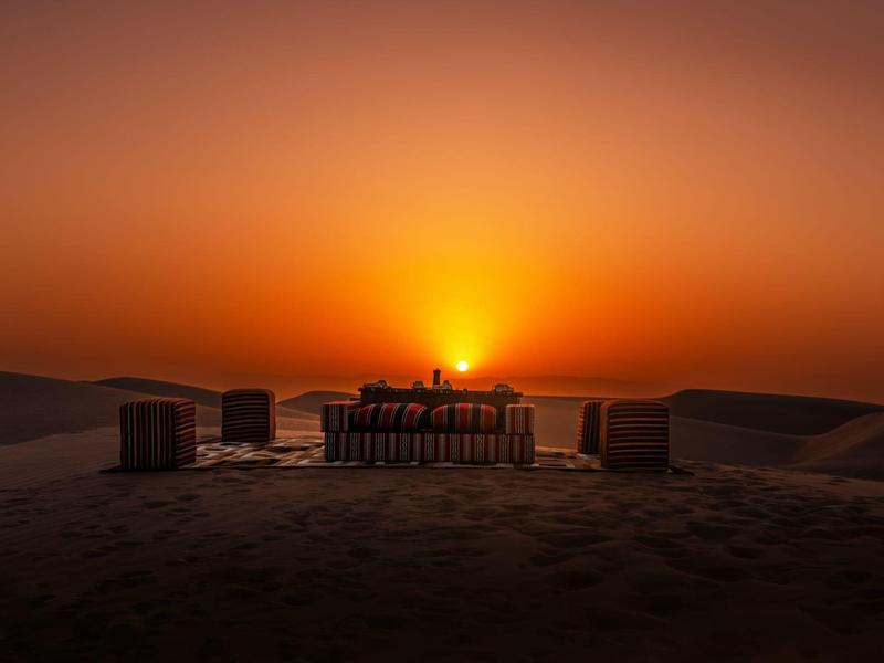 Sonnenuntergang über Wüstenlandschaft mit Sitzgelegenheiten und Tischen im Vordergrund.