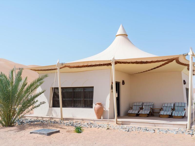 Einzelnes Zelt mit weißer spitzer Dachkonstruktion in Wüstenlandschaft bei klarem Himmel.