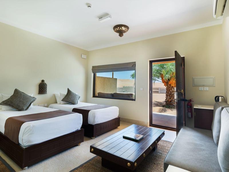 Zweibettzimmer mit Holzrahmen, großem Fenster, Zugang zur Terrasse und grauer Couch.