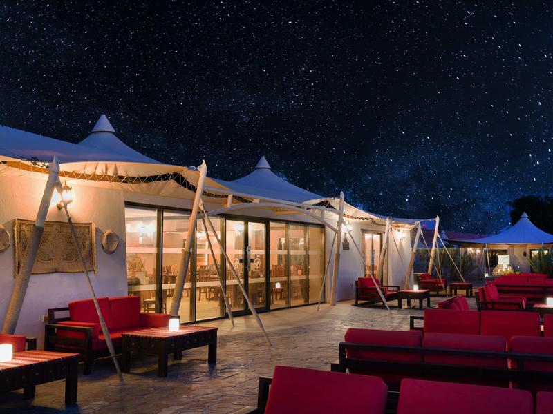 Beleuchtete Outdoor-Lounge mit roten Sofas und Sternenhimmel im Hintergrund bei Nacht.