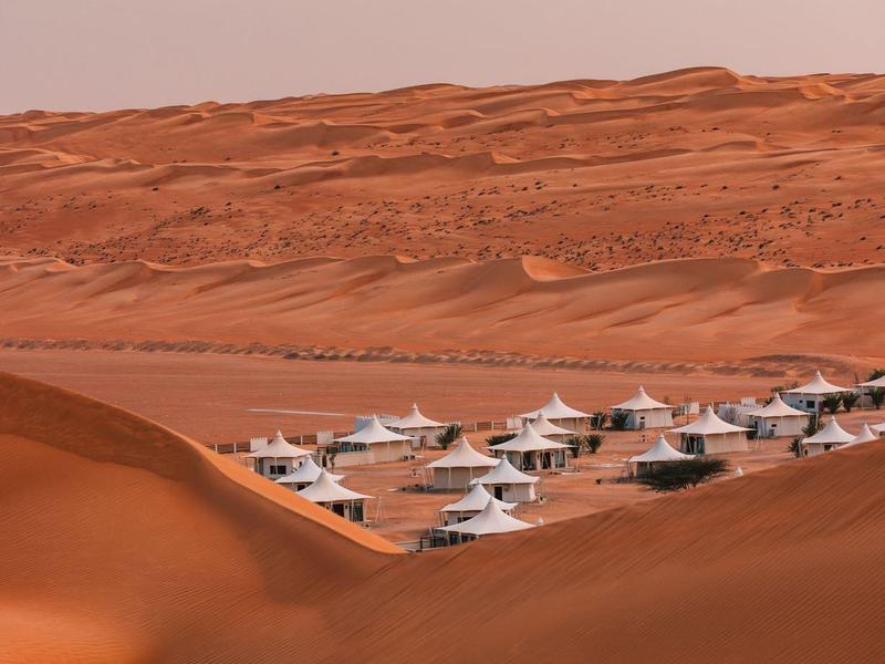 Rote Sanddünen mit weißen Zelten in einer Wüstenlandschaft unter bewölktem Himmel.