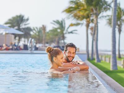 Paar entspannt sich im Pool mit Blick auf Palmen und Sonne.