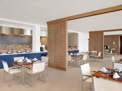 Nowoczesna jadalnia z drewnianymi stolikami i białymi krzesłami w jasnej, otwartej przestrzeni.