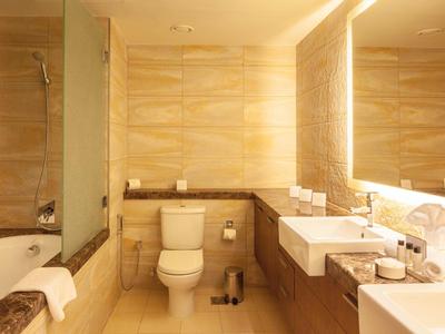 Jasna łazienka hotelowa z toaletą, dwoma umywalkami i wanną z zasłoną prysznicową.