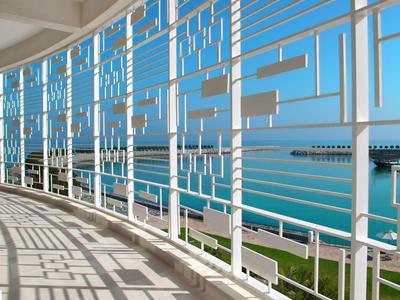 Widok na morze przez geometryczną białą metalową balustradę na balkonie hotelowym.