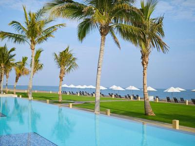 Basen infinity z widokiem na morze, palmy i leżaki z parasolami na trawniku.