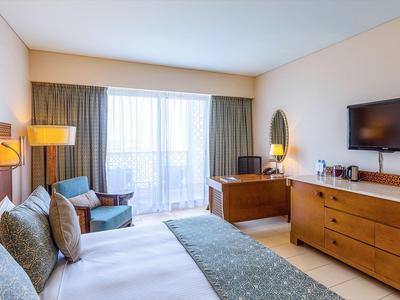 Jasny pokój hotelowy z podwójnym łóżkiem, miejscem do siedzenia i telewizorem z płaskim ekranem.