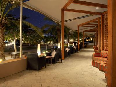 Zadaszony salon na zewnątrz z stołami i krzesłami w pobliżu palm nocą.