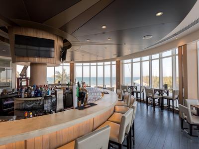 Wnętrze nowoczesnego baru hotelowego z ladą i miejscami do siedzenia przy dużych oknach.