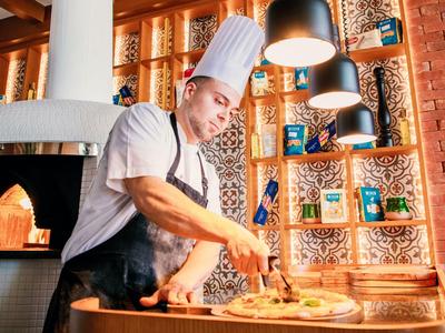 Ein Koch in Weißer Mütze bereitet in warmer, dekorativer Restaurantumgebung Essen zu.