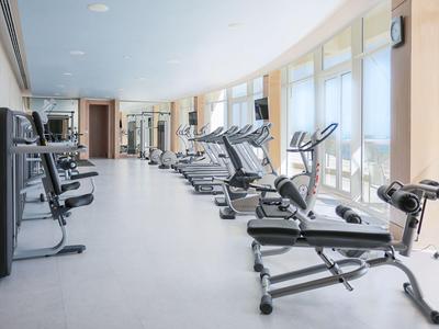 Helles Fitnessstudio mit Laufbändern und Trainingsgeräten neben großen Fenstern.