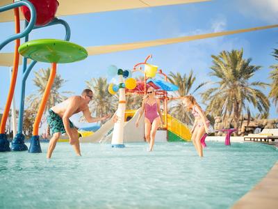 Dzieci bawiące się w płytkim basenie z kolorowymi atrakcjami wodnymi i palmami