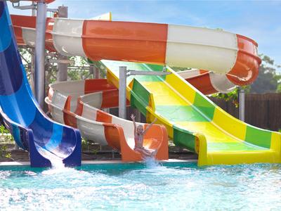 Kilka kolorowych zjeżdżalni wodnych prowadzi do basenu pod jasnym niebem.