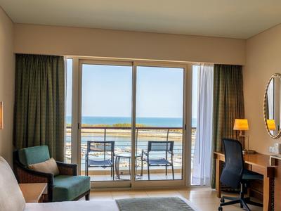 Pokój hotelowy z balkonem, dwoma krzesłami i widokiem na morze.