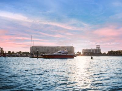 Żaglówka na spokojnej wodzie o zachodzie słońca z nowoczesnymi budynkami w tle.